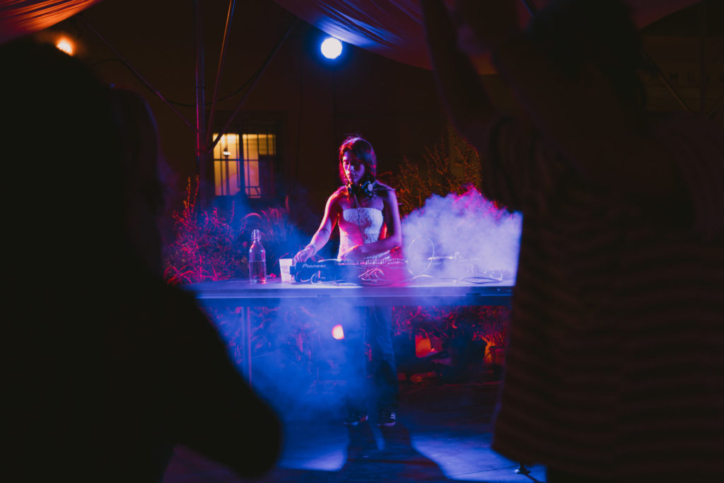La DJette ven3mo mixe des sons sur sa table. Elle est entourée de lumières violettes presque fluorescentes.