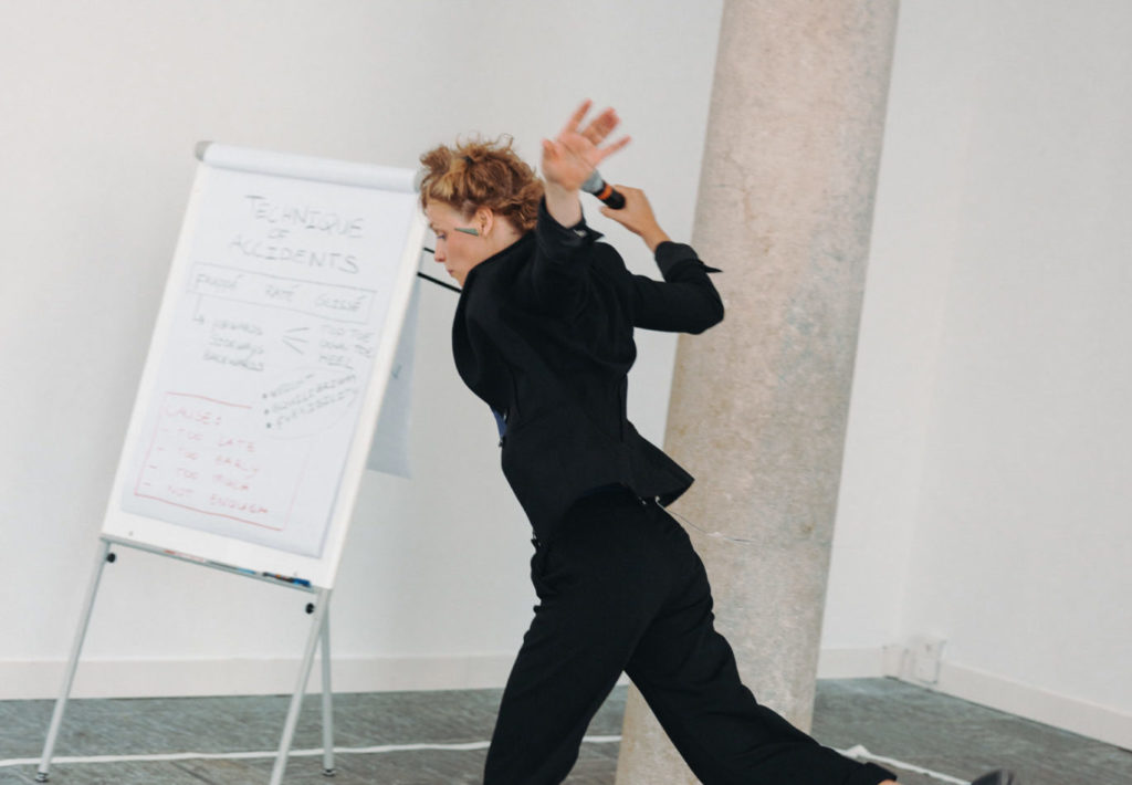 The artist Salomé Mooij wears black clothes. She has her arms in the air and experiments movements of stumble.