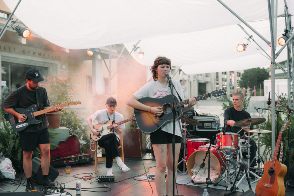 On voit un groupe de musique sur une scène. La chanteuse clair my flair est devant à droite et on aperçoit les trois autres musiciens derrière autour d'elle.