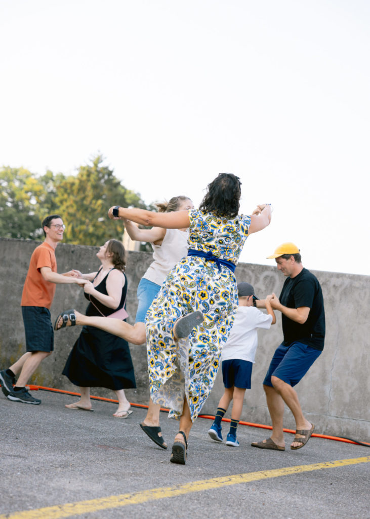 We see couples of people dancing the waltz. In the foreground we see a woman from behind who has only the tip of her foot touching the floor. She is elevated in the air.