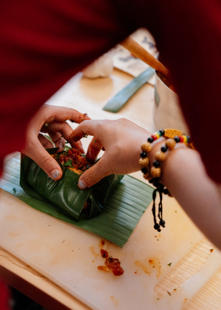 We can see two hands cooking a meal on a bamboo leaf. The hands are stuffing a bamboo leaf with a salted mixture.