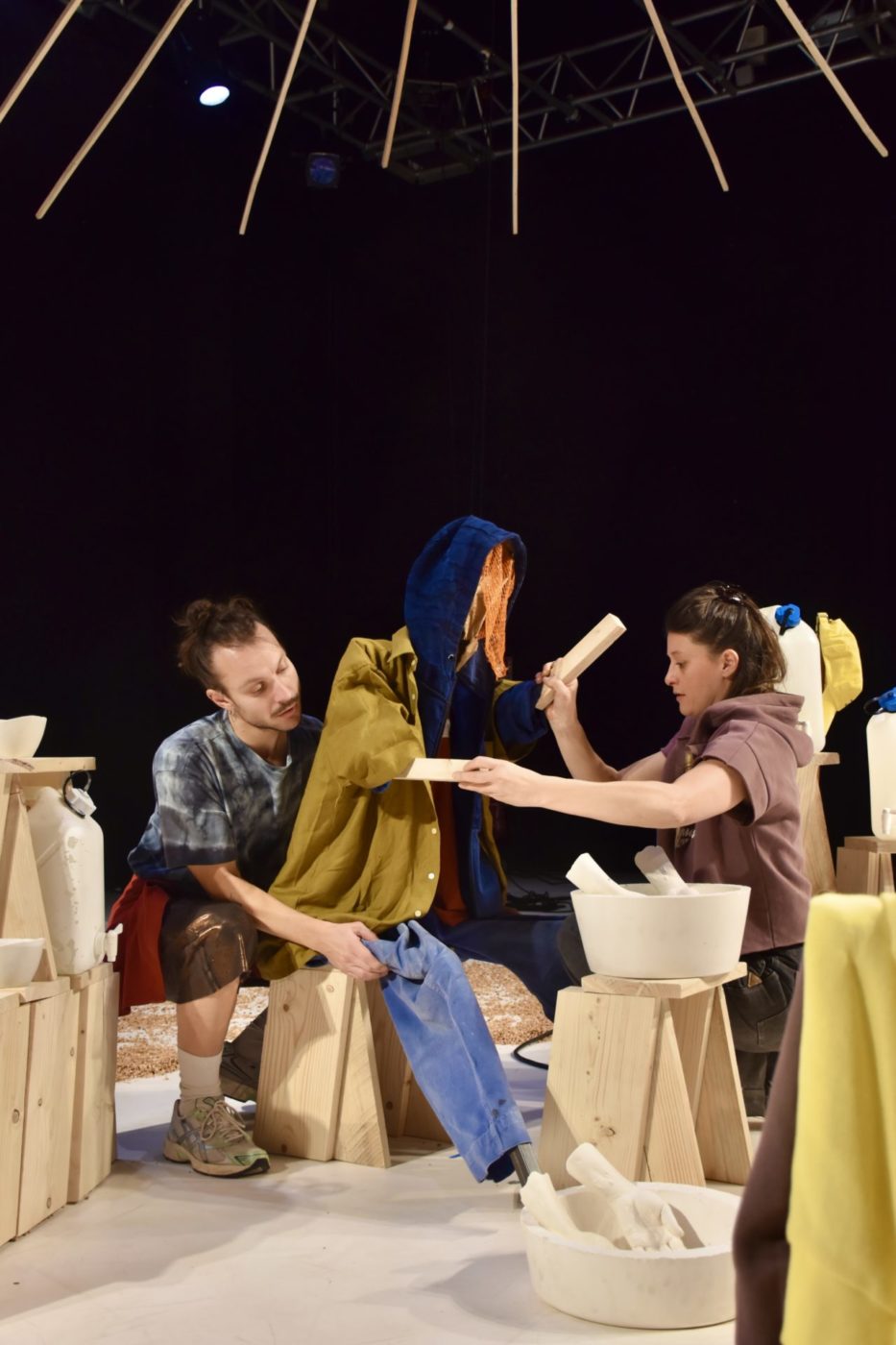 Deux personnes du spectacle sont en train d'habiller une grande marionnette (de taille humaine) avec des vêtements d'humain.