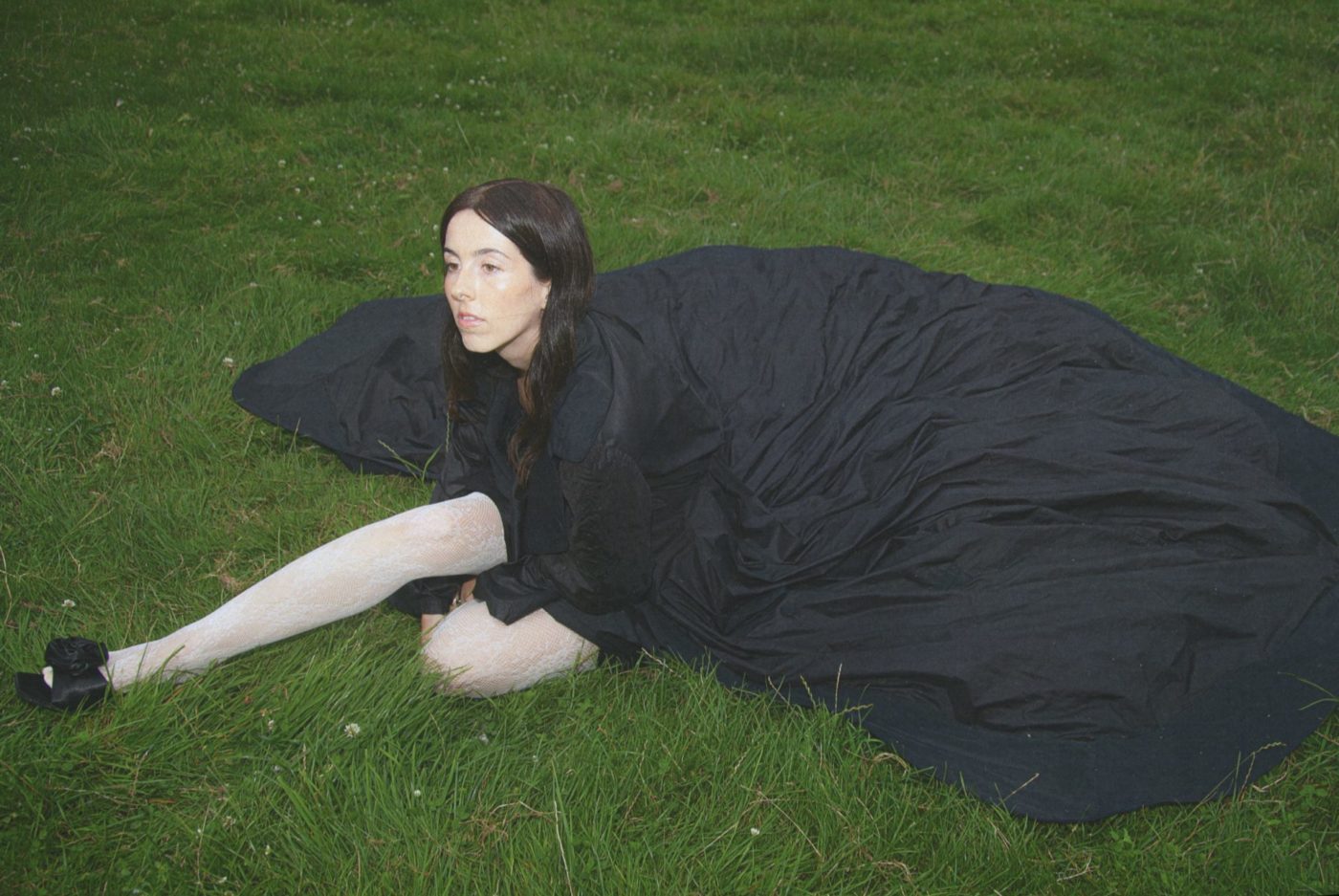 Verde Prato est assise dans l'herbe avec une grande robe noire.