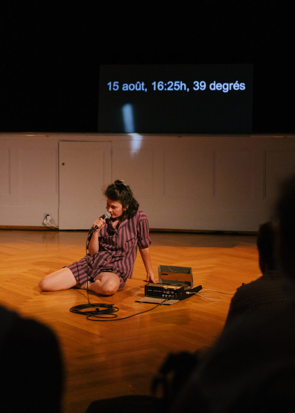 The artist Annina Polivka sits on the floor, before the scene. She has a microphone in her hand, in which she talks.