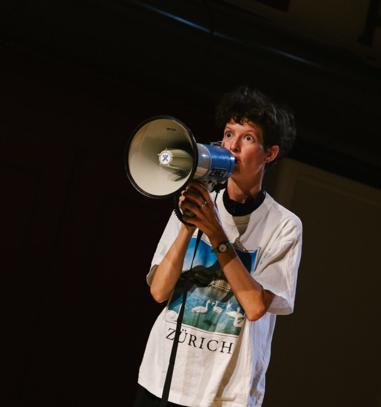 Elise Perrin porte un t-shirt souvenir de Zürich. Elle parle dans un mégaphone.
